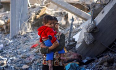 A Palestinian boy carrying a baby stands at a site of a destroyed building in Rafah