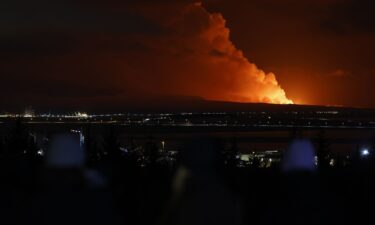 People watch as the night sky is illuminated caused by the eruption of a volcano on the Reykjanes peninsula of south-west Iceland seen from the capital city of Reykjavik