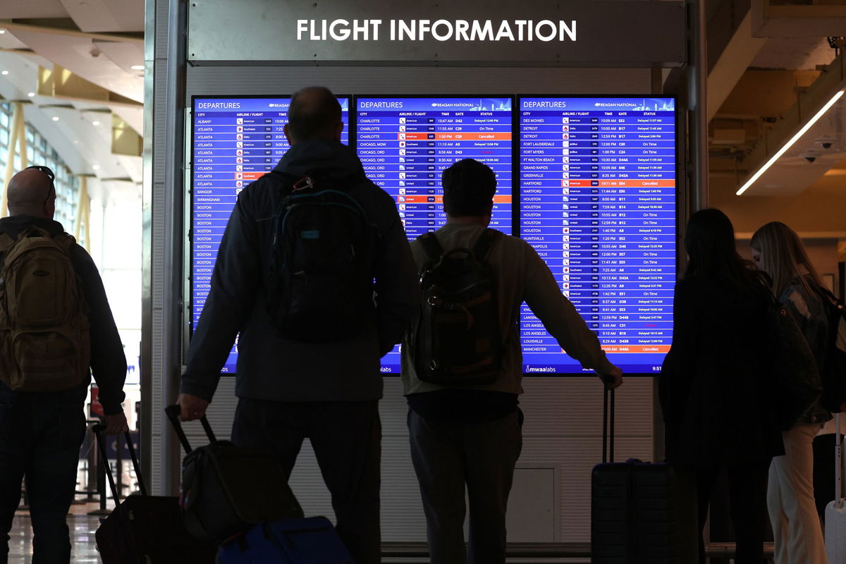 <i>Alex Wong/Getty Images</i><br/>Travelers looks at a flight information board at Ronald Reagan Washington National Airport in 2023.