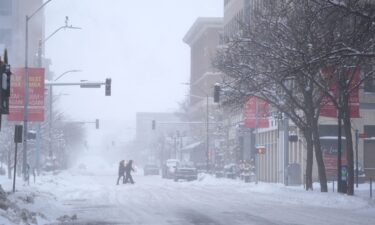 Pedestrians cross the street in snowy conditions on Friday