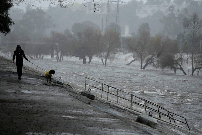 A man walks his dog on the edge of the Los Angeles River, carrying stormwater downstream on February 4 in Los Angeles. The second of back-to-back atmospheric rivers battered California, flooding roadways and knocking out power to hundreds of thousands.