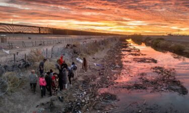 Immigrants wait next to razor wire after crossing the Rio Grande into El Paso
