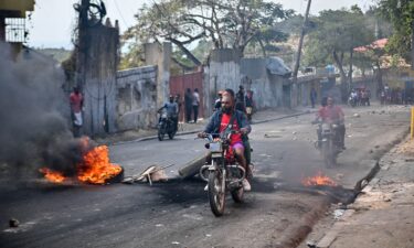 Motorcyclists pass burning tires during a demonstration calling for the resignation of Prime Minister Ariel Henry