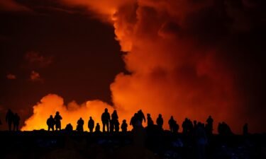People on the outskirts of Reykjavik take pictures of the orange colored sky as molten lava flows out from a fissure on the Reykjanes peninsula north of the evacuated town of Grindavik