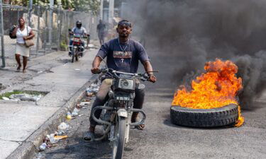 A motorcyclist passes burning tires during a demonstration against CARICOM