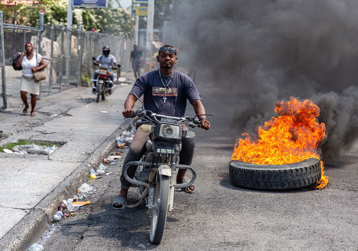 <i>Guerinault Louis/Anadolu/Getty Images via CNN Newsource</i><br/>A motorcyclist passes burning tires during a demonstration against CARICOM