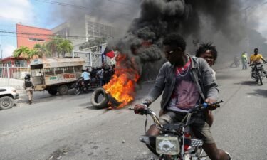 People drive past a burning blockade as demonstrators hold a protest calling for the resignation of Haitian Prime Minister Ariel Henry outside the Canadian Embassy