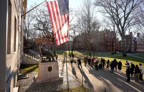People take photographs near a John Harvard statue