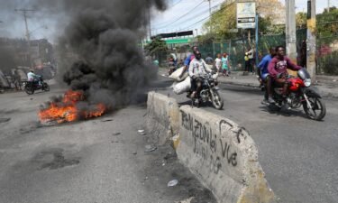 Motorists pass by a burning barricade during a protest as the government said it would extend a state of emergency for another month after an escalation in violence from gangs in Port-au-Prince