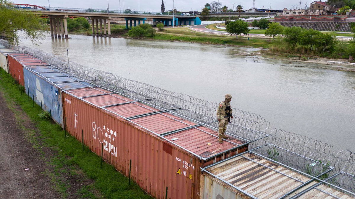 <i>John Moore/Getty Images via CNN Newsource</i><br/>A Texas National Guard soldier stands atop a barrier of shipping containers and razor wire while guarding the US-Mexico border on March 17