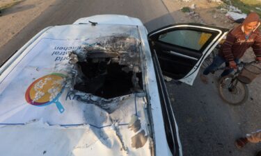 A Palestinian man rides a bicycle past a damaged vehicle where employees from the World Central Kitchen were killed in an Israeli airstrike