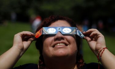 A woman uses eclipse glasses to observe an annular solar eclipse at the Bicentenario Park in Antiguo Cuscatlan