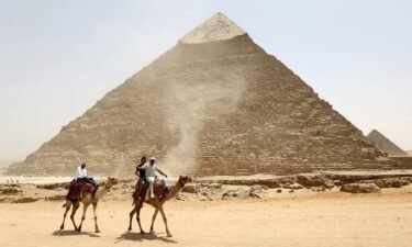 Tourists ride on camels next to the Pyramid of Khufu on the Great Pyramids of Giza
