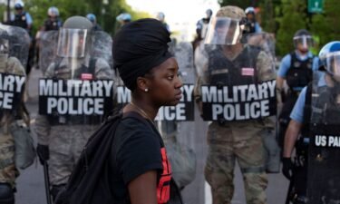 A demonstrator walks in front of a row of military police members wearing riot gear as they push back demonstrators outside of the White House