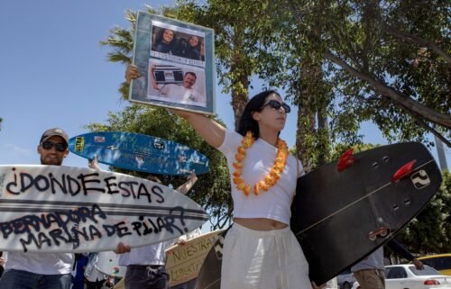 A demonstrator holds photos of the surfers during a protest in Ensenada