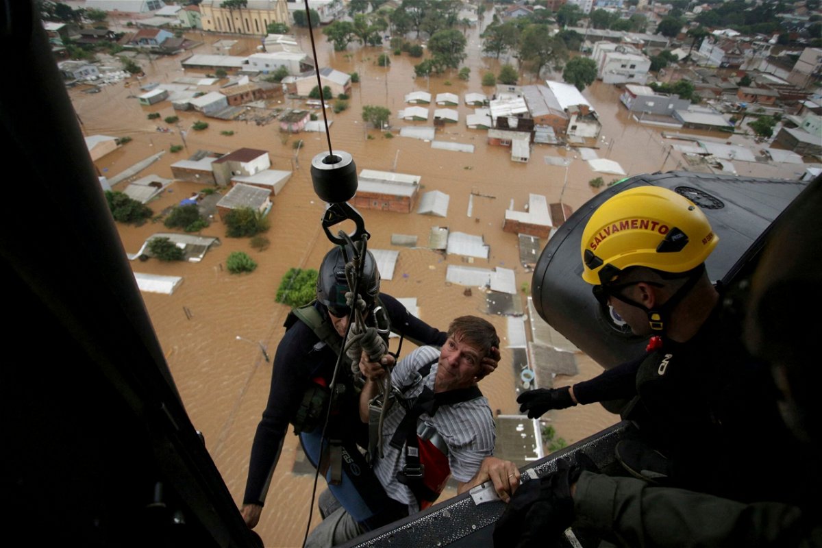<i>Renan Mattos/Reuters via CNN Newsource</i><br/>Military firefighters rescue a man using a helicopter.