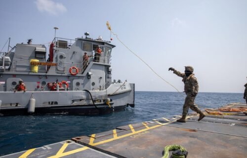 A U.S. Army Soldier tosses a line to an Army tug vessel from the Roll-On