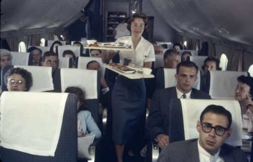 A Pan American Airline flight attendant serves trays of food to passengers on a plane in 1958.