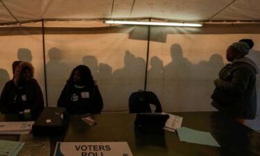 Electoral workers prepare to open the voting station as voters line up to cast their ballot for general elections in Alexandra