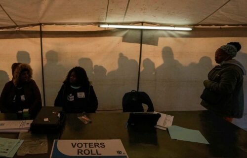 Electoral workers prepare to open the voting station as voters line up to cast their ballot for general elections in Alexandra