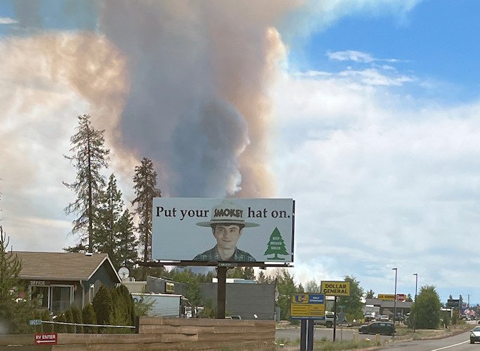 A 'Put Your Smokey Hat On - Keep Oregon Green' billboard in La Pine has drawn added attention this week, juxtaposed with the smoke plumes from the Darlene 3 Fire.
