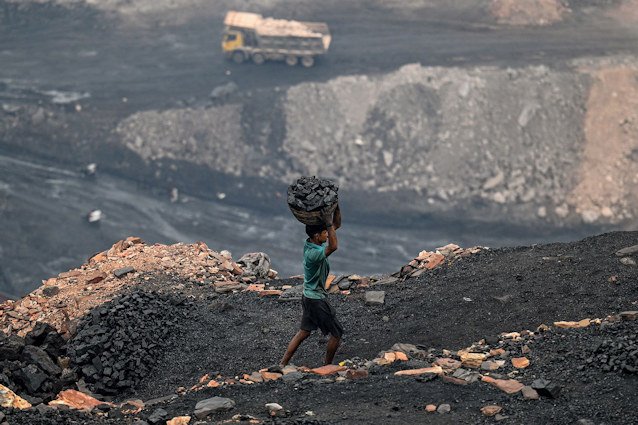 A coal picker carries coal from near an open cast mining site on the outskirts of Dhanbad, India in July 2023.