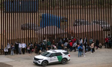 Migrants and asylum seekers wait to be processed by the Border Patrol between fences at the US-Mexico border seen from Tijuana
