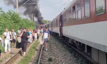 Smoke billows from a fire while people evacuate from a train