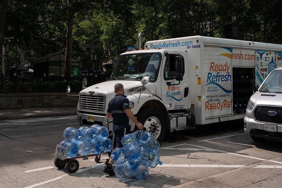 <i>Adam Gray/Bloomberg/Getty Images via CNN Newsource</i><br/>A worker wheels empty water jugs to a truck during high temperatures in New York on June 20.