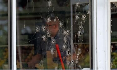 Damage can be seen to a front window as law enforcement officers work the scene of a shooting at the Mad Butcher grocery store in Fordyce
