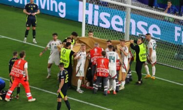 Players and stewards hold sheets to shield Barnabás Varga while he receives medical treatment.