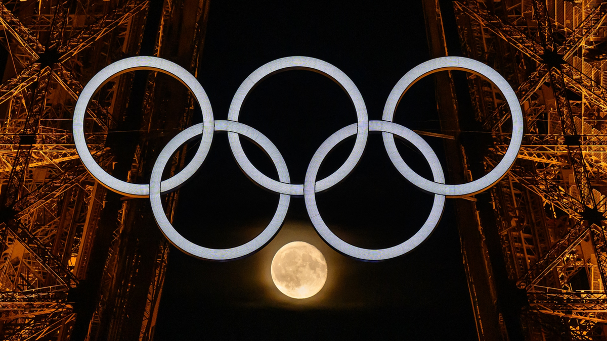 The moon is pictured through the Olympic rings displayed on the Eiffel tower