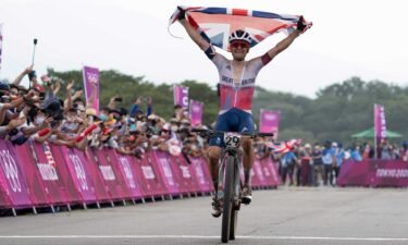 Tom Pidcock holds up Great Britain flag while riding mountain bike