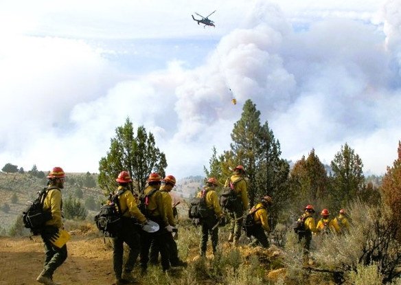 Firefighters head in to construct fire line in triple-digit heat as a helicopter flies overhead to cool off hot spots with water on the Falls Fire, currently burning on the Malheur National Forest. 