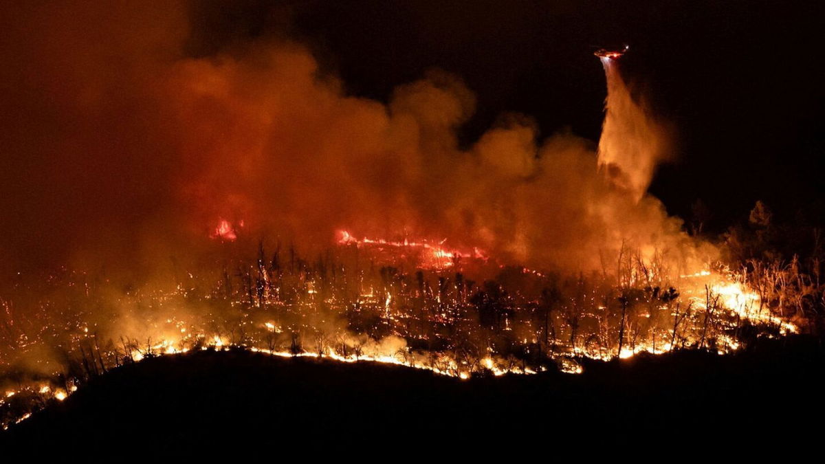 <i>Carlos Barria/Reuters via CNN Newsource</i><br/>A helicopter drops water over the Thompson Fire as firefighters continue battling fire into the night near Oroville