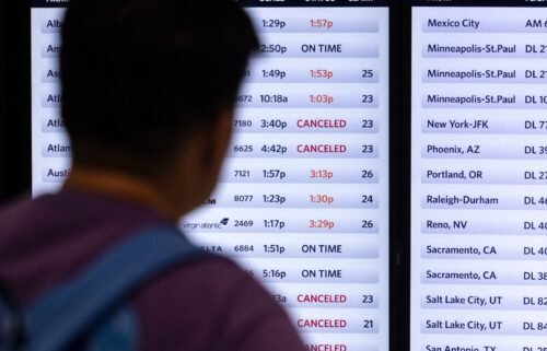 A traveler looks at a screen displaying delayed and canceled flights in Terminal 2