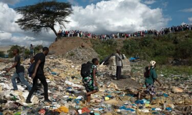 People walk among rubbish as others stand on the edge of a dumpsite where six bodies were found at the landfill in Mukuru slum