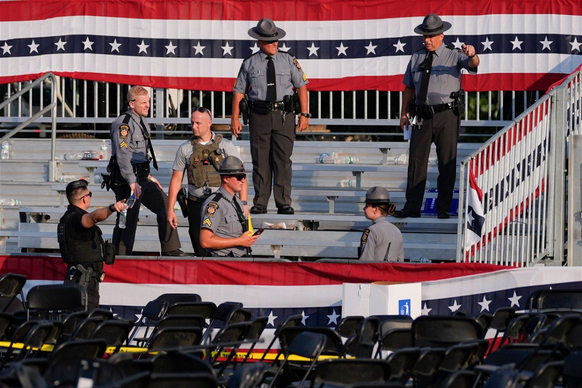 <i>Evan Vucci/AP via CNN Newsource</i><br/>Law enforcement officers work at the campaign rally site for Republican presidential candidate former President Donald Trump is empty and littered with debris July 13