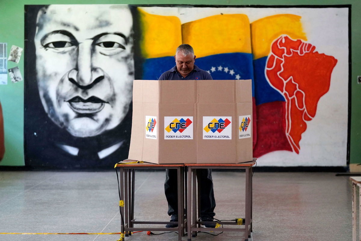 <i>Fernando Vergara/AP via CNN Newsource</i><br/>A voter chooses his candidate in front of a mural of late Venezuelan President Hugo Chavez during the presidential election in Caracas