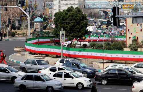 Cars drive past a wall covered by a banner in the colours of the national flag in Tehran