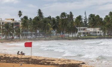 Tourists sit on La Pared beach as Tropical Storm Ernesto whips up surf near Luquillo