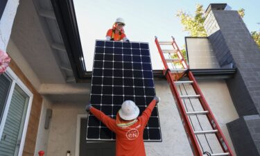 Workers install solar panels on the roof of a home in Poway