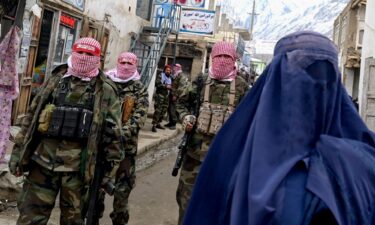 Taliban guards stand beside a burqa-clad woman on a street at a market in the Baharak district of Badakhshan province