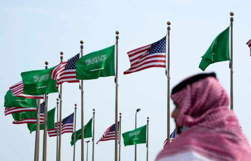 A man stands under American and Saudi Arabian flags at a square in Jeddah