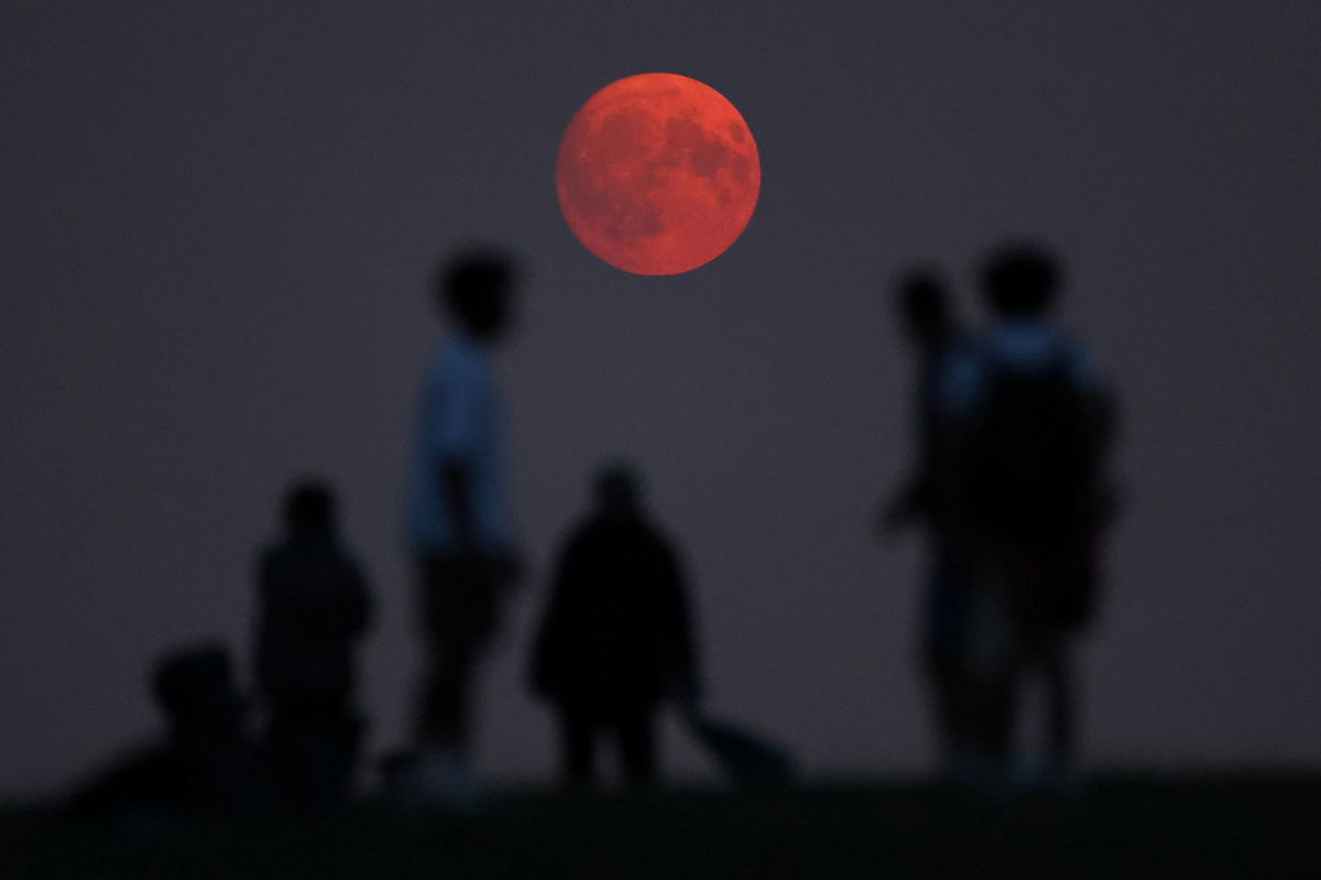 <i>Toby Melville/Reuters via CNN Newsource</i><br/>People view the moon as it rises