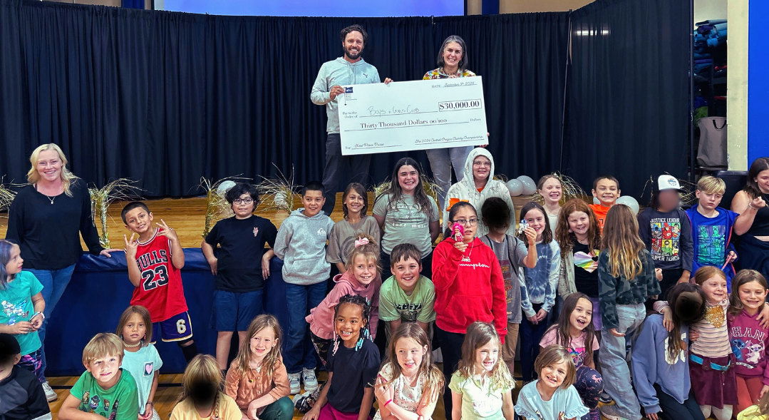 Celebrating a Major Win! The Boys & Girls Clubs of Bend (BGCB) receives a $30,000 check won by the team from Beaver Coach Sales & Service at the inaugural Hayden Homes - Central Oregon Charity Championship Golf Tournament. Pictured on stage, Craig Melton of Beaver Coach Sales & Service and Bess Goggins, CEO of BGCB, share the exciting moment with Club members during a special event at BGCB.