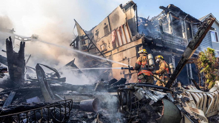 Firefighters spray water from fire hoses onto a smoldering house after a plane crashed into a row of townhomes in Fairview on Saturday, August 31.