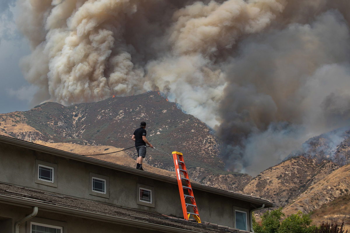 <i>Apu Gomes/Getty Images via CNN Newsource</i><br/>A man waters the roof of his home as the Line Fire burns in the foothills of the San Bernardino Mountains