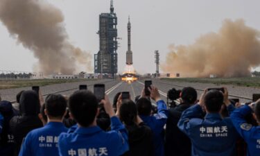 A crowd watches three astronauts blast off onboard the Long March-2F at China's Jiuquan Satellite Launch Center on May 30