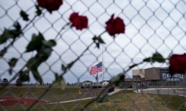 Roses hang from a fence and the American flag is lowered to honor the victims of the November 30